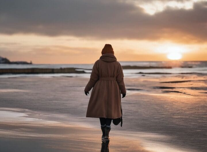 una mujer de espaldas muy abrigada caminando en la orilla del mar mucho frio al atardecer png 1 1